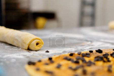 Foto de La cocina en la panadería - el proceso de fabricación de cinabriones, mujer panadero utiliza chocolate en gránulos para hornear - Imagen libre de derechos