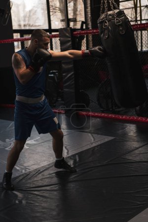 Foto de Boxeo gimnasio un boxeador entrena sus golpes golpeando saco de boxeo - Imagen libre de derechos
