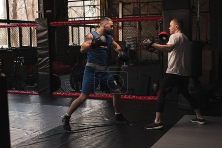Téléchargez les photos : Boxer pratique ses coups avec son entraîneur dans le gymnase de boxe - en image libre de droit