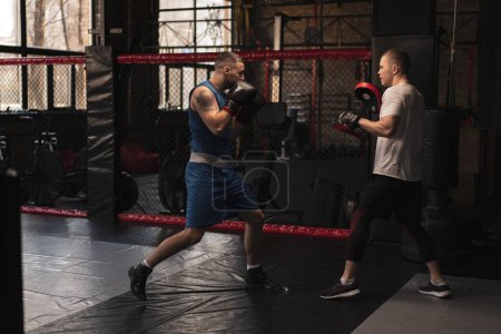 Téléchargez les photos : Boxer pratique ses coups avec son entraîneur dans le gymnase de boxe - en image libre de droit
