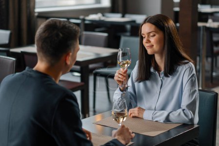 Téléchargez les photos : Un rendez-vous dans un restaurant d'hôtel un homme et une femme boivent du vin blanc dans des verres visage d'une fille souriante - en image libre de droit