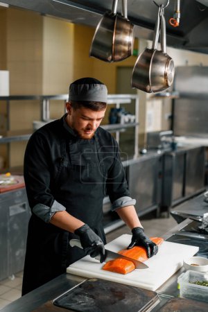 Téléchargez les photos : Cuisine professionnelle dans le restaurant de l'hôtel chef coupe une grande carcasse de saumon frais avec un couteau - en image libre de droit