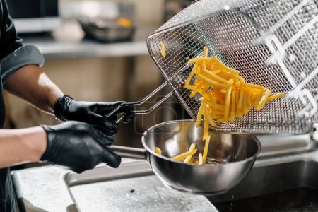 Photo for Professional kitchen in restaurant of the hotel the chef takes out delicious french fries from the fryer - Royalty Free Image