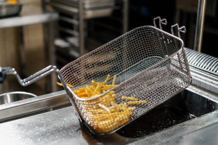 Foto de Cocina profesional en el restaurante del hotel el chef saca deliciosas papas fritas de la freidora - Imagen libre de derechos