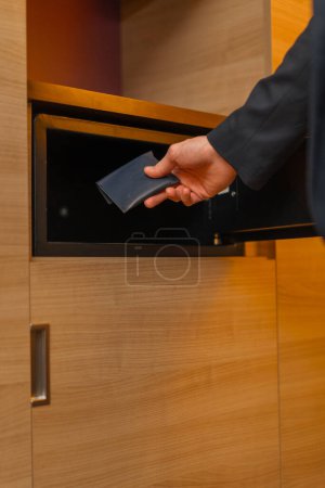 Foto de Primer plano de la mano de un hombre poniendo una billetera con dinero en una caja fuerte en la habitación de hotel almacenamiento de valores - Imagen libre de derechos