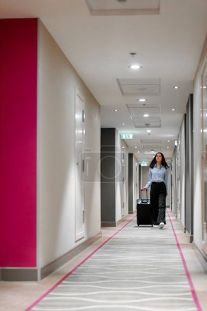 Téléchargez les photos : Une fille avec une valise marche dans le couloir de l'hôtel femme d'affaires en voyage le concept de voyage - en image libre de droit