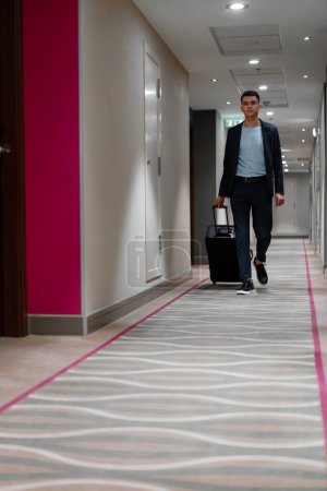 Téléchargez les photos : Un homme avec une valise marche dans le couloir de l'hôtel une vue d'un homme d'affaires en voyage - en image libre de droit