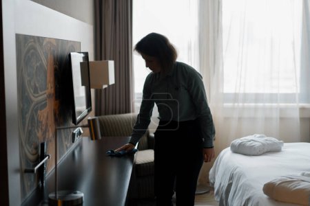 Téléchargez les photos : Femme de ménage en uniforme époussetant tout en préparant luxe chambre d'hôtel invités nettoyage et concept de voyage - en image libre de droit