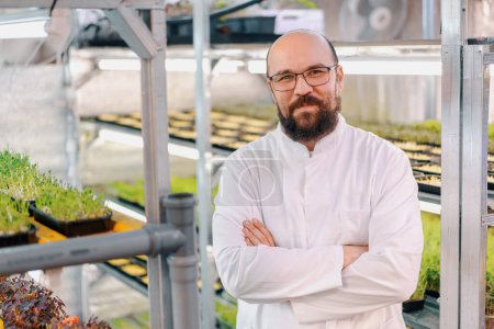 Téléchargez les photos : Portrait de jardinier masculin souriant dans des lunettes et un manteau blanc ferme microverte Alimentation végétalienne saine germination des plantes biologiques - en image libre de droit