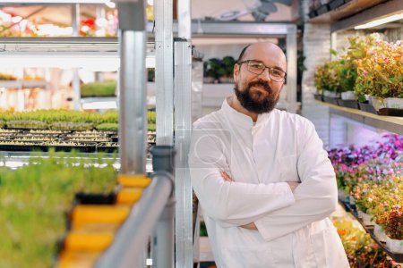 Foto de Retrato de jardinero masculino sonriente en gafas y capa blanca granja microverde Alimento vegano saludable Germinación orgánica de plantas - Imagen libre de derechos