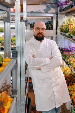 Foto de Retrato de jardinero masculino serio en gafas y capa blanca granja microgreen Alimento vegano saludable Germinación orgánica de plantas - Imagen libre de derechos