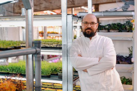 Foto de Retrato de jardinero masculino sonriente en gafas y capa blanca granja microverde Alimento vegano saludable Germinación orgánica de plantas - Imagen libre de derechos