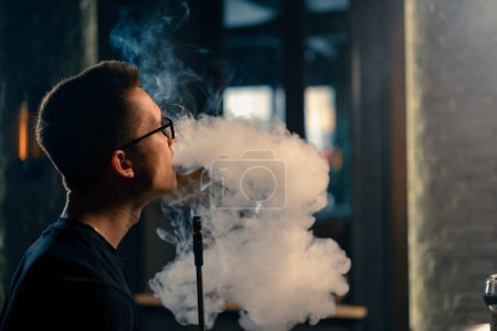 Téléchargez les photos : Un narguilé à lunettes fume un tuyau traditionnel de narguilé Un homme exhale de la fumée dans un café narguilé ou un bar-salon gros plan - en image libre de droit