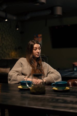 Photo for A girl with hot tea in a cup sitting in a hookah room listens attentively to interlocutor the concept of relaxation - Royalty Free Image