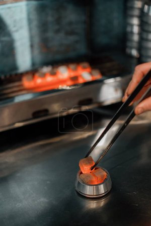 Photo for Coal for hookah is roasted on fire the hookah worker turns the coal with special tongs - Royalty Free Image