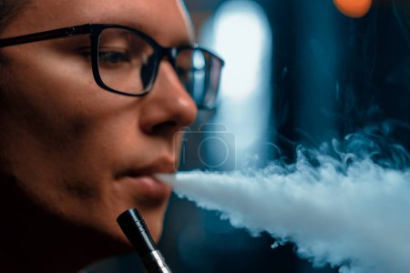 Téléchargez les photos : Gros plan homme narguilé dans des lunettes fumant une pipe traditionnelle narguilé homme expirant fumée dans le café narguilé ou bar lounge - en image libre de droit