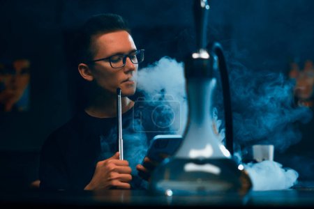 Photo for Hookah man in glasses smoking a traditional hookah pipe Man exhaling smoke in hookah cafe or lounge bar - Royalty Free Image