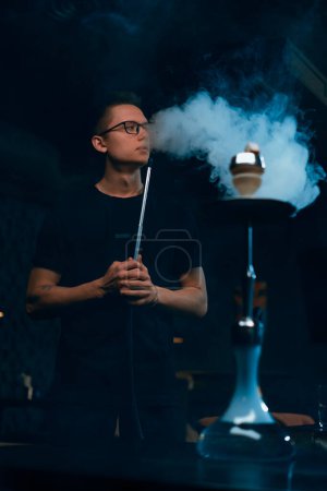 Photo for Hookah man in glasses smoking a traditional hookah pipe Man exhaling smoke in hookah cafe or lounge bar - Royalty Free Image