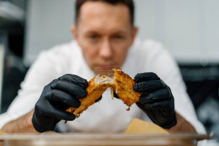 Photo for A chef in professional kitchen tears apart baked pieces of chicken fillet in breadcrumbs with his hands - Royalty Free Image
