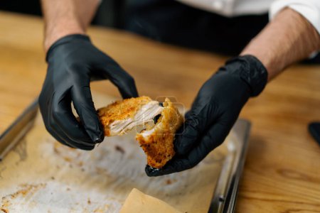 Téléchargez les photos : Un chef dans la cuisine professionnelle déchire morceaux cuits de filet de poulet dans la chapelure avec ses mains - en image libre de droit