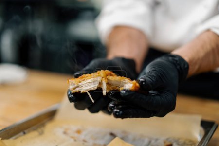 Photo for A chef in professional kitchen tears apart baked pieces of chicken fillet in breadcrumbs with his hands - Royalty Free Image