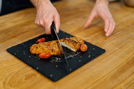 Téléchargez les photos : Chef cuisinier dans la cuisine professionnelle coupe morceaux cuits filet de poulet dans la chapelure - en image libre de droit