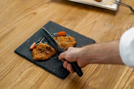 Foto de Cocinero cocina profesional corta trozos horneados filete de pollo en migas de pan - Imagen libre de derechos