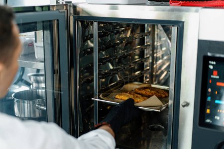 Téléchargez les photos : Chef cuisinier dans une cuisine professionnelle prend des morceaux cuits de filet de poulet dans la chapelure du four - en image libre de droit