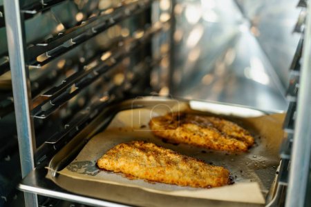Photo for Chef cooking in a professional kitchen baked pieces chicken fillet in breadcrumbs in oven - Royalty Free Image