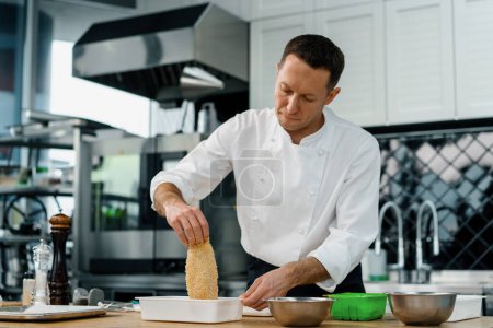 Téléchargez les photos : Chef cuisinier dans la cuisine professionnelle trempettes morceaux filet de poulet dans la chapelure processus de cuisson - en image libre de droit