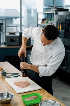 Foto de Chef de cocina en una cocina profesional añade condimentos trozos de filete de pollo picado cocinar pollo empanado - Imagen libre de derechos