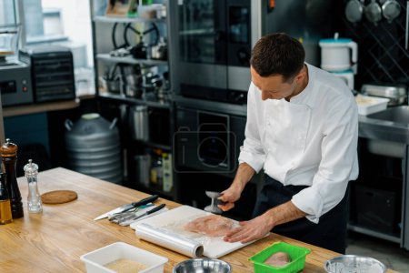 Foto de Chef cocina profesional cocina golpeando filete de pollo con carne mallet concepto de comida saludable - Imagen libre de derechos