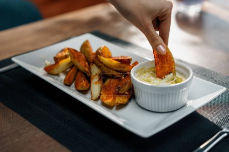 Foto de Un plato en un restaurante de patatas al horno con especias en la palma de la mano sumergido en salsa de crema agria de cerca - Imagen libre de derechos