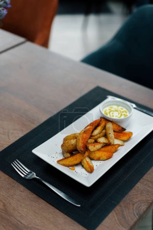 Foto de Plato de restaurante salsa de crema agria y cuñas de patata al horno con especias en plato sobre la mesa - Imagen libre de derechos