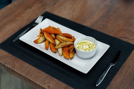 Téléchargez les photos : Plat restaurant sauce à la crème sure et des quartiers de pommes de terre cuites avec des épices dans l'assiette sur la table - en image libre de droit