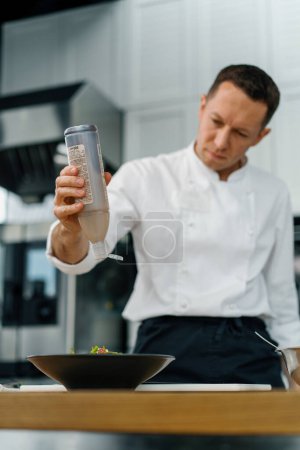 Photo for Professional kitchen the chef pours red sauce on salad with pear and cheese mixes the ingredients of healthy food - Royalty Free Image