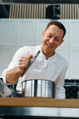 Photo for Professional kitchen satisfied chef the chef lifts the lid of the pot and checks the readiness of dish cooking - Royalty Free Image