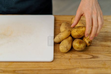 Photo for A professional kitchen cook cuts potato wedges with a knife to cook them in oven raw potatoes - Royalty Free Image