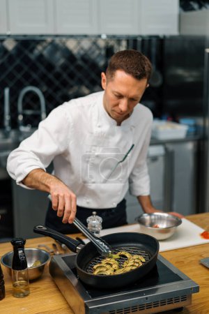 Téléchargez les photos : Chef de cuisine professionnel flips avocat vert frais avec pinces sur la poêle légumes concept d'alimentation saine - en image libre de droit