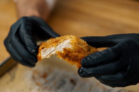 Photo for A chef in a professional kitchen tears apart baked pieces of chicken fillet in breadcrumbs with his hands - Royalty Free Image