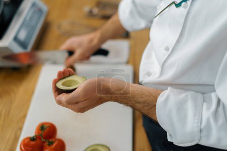 Foto de Cocinero profesional limpia aguacate verde fresco con un cuchillo elimina la piel de cerca - Imagen libre de derechos