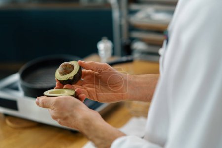 Téléchargez les photos : Chef de cuisine professionnel nettoie avocat vert frais avec un couteau enlève la peau gros plan - en image libre de droit
