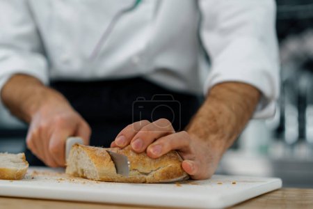Foto de Profesional moderno restaurante cocina chef corte recién horneado pan listo de horno tostado con cuchillo de cerca - Imagen libre de derechos