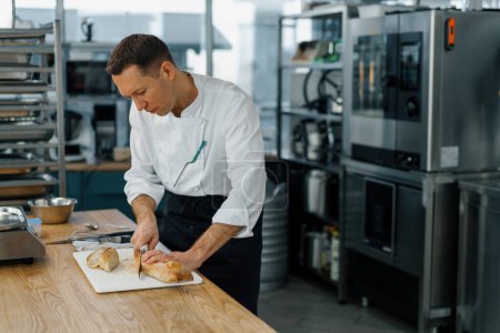Téléchargez les photos : Cuisine moderne professionnelle dans le chef restaurant coupe pain frais cuit au four prêt à partir de pain grillé au four avec couteau - en image libre de droit