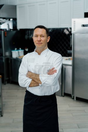 Téléchargez les photos : Cuisine professionnelle souriant et satisfait chef manteau blanc debout avec des bras croisés portrait - en image libre de droit