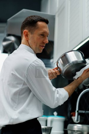 Téléchargez les photos : Gai chef professionnel dans la cuisine laver la vaisselle sale dans l'évier après la cuisson concept de nourriture - en image libre de droit