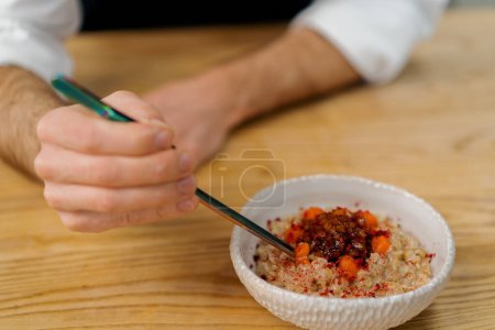 Photo for Professional kitchen chef lays pieces caramelized apple in freshly cooked oatmeal breakfast food concept - Royalty Free Image