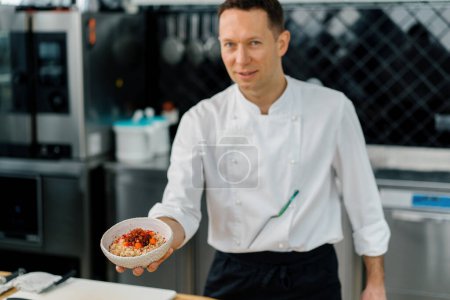 Téléchargez les photos : Cuisine professionnelle chef satisfait montrant fraîchement préparé flocons d'avoine avec petit déjeuner aux fruits caramélisés close-up - en image libre de droit