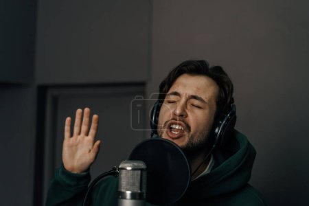 Téléchargez les photos : Chanteur avec écouteurs et microphone enregistrement émotionnel d'une nouvelle chanson en studio d'enregistrement professionnel - en image libre de droit