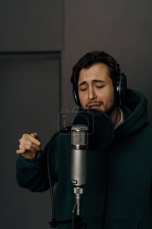 Foto de Cantante con auriculares y micrófono grabando emocionalmente una nueva canción en un estudio de grabación profesional - Imagen libre de derechos